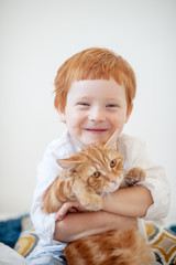 Funny red-haired boy in white bed with a red cat