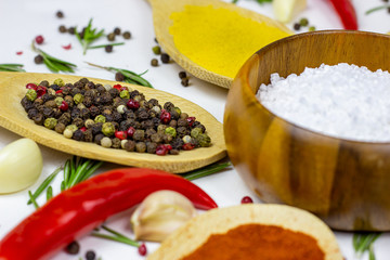 Variety of spices and seasonings (indian curry, different pepper, paprika powder, salt, dry ginger and curcuma) for cooking in wooden spoons on white kitchen table background.