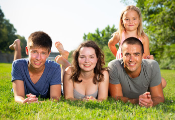 Portrait of positive family on green lawn in summer park