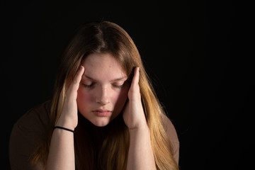 Sad teen girl on a black background with head in hands.