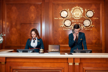 Working process. Attractive executives at the reception desk of a hotel. Young man answering phone call - obrazy, fototapety, plakaty