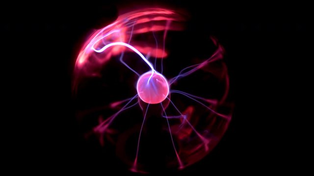 A female hand touches a plasma ball giving out small lightning bolts. Experiments with electricity in the dark.