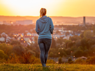 Rear view of woman enjoying beautiful sunset with the city of Augsburg in the background