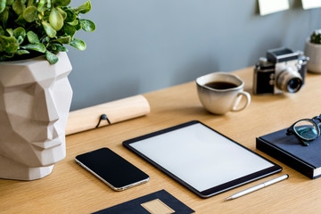 Modern business composition on the wooden desk with mock up tablet screen, plant, photo camera, notes, mobile phone and office supplies in stylish concept of home decor.