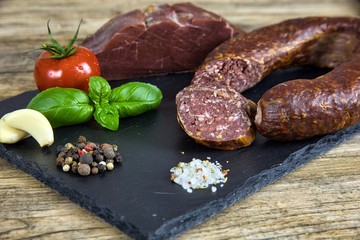 Smoked salami homemade with spices on a slate plate on a rustic wooden background