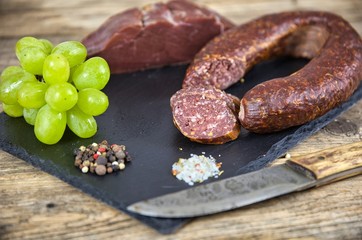 Smoked salami homemade with spices on a slate plate on a rustic wooden background