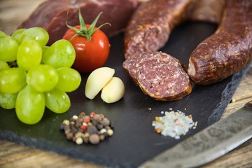 Smoked salami homemade with spices on a slate plate on a rustic wooden background