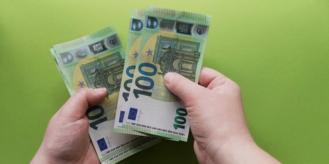 Caucasian hands holding and counting a bundle of 100 Euro banknotes issued in 2019 on green background.Concept of limiting cash payments to prevent the spread of coronavirus.Soft focus, copy space