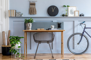 Scandinavian interior design of open space with wooden desk, modern chair, wood paneling with shelf, plant, carpet, bicycle, office supplies and elegant personal accessories.