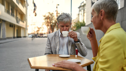 Enjoy the little things. Stylish senior couple sitting together at coffee shop outdoors and enjoying coffee