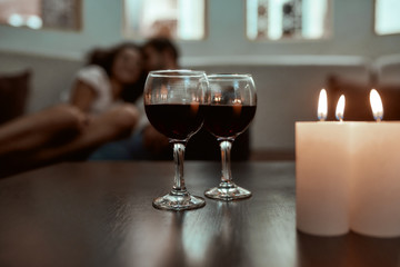 Romance hold a relationship tight. Wine glasses and candles on table with couple relaxing in the background on couch