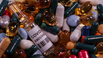 Close up of Coronavirus vaccine in ampoule surrounded by hundreds of colorful pills. Concept:...