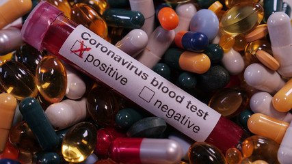 Positive coronavirus blood test surrounded by hundreds of colorful pills. Concept: COVID-19 virus...