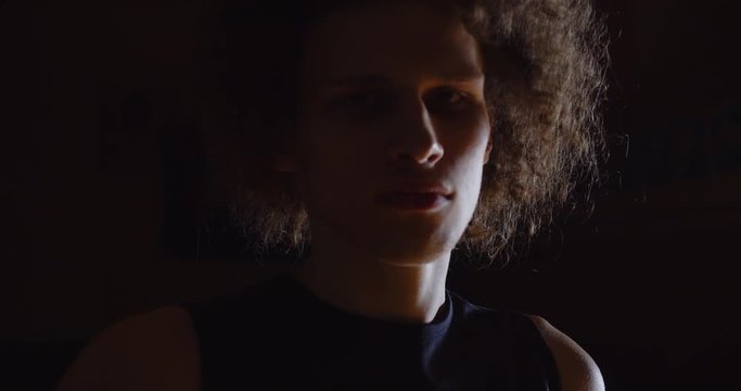 Close-up Popular curly-haired Caucasian basketball player portrait serious look at camera photographers flash holds ball professional darkness