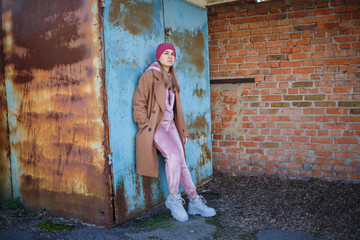 stylish girl model in a brown coat, pink suit and gray boots on the city ruins. The trends of modern fashion. Fashionable image