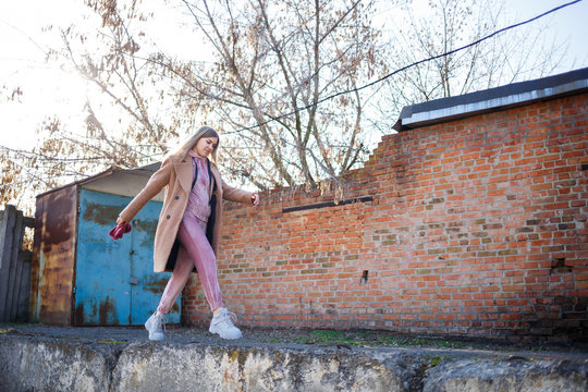 stylish girl model in a brown coat, pink suit and gray boots on the city ruins. The trends of modern fashion. Fashionable image