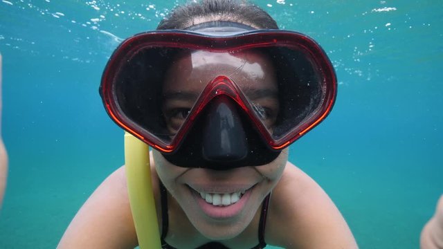 Underwater girl in snorkeling mask and bikini holding the camera with big smile