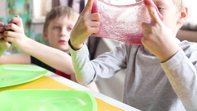 Anti-stress toys for children. Cute kid enjoying a slime toy. A boy sits at a table at home. The child wrinkles slime. Children play with colorful slimes.