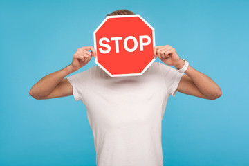 Portrait of unknown man in white t-shirt covering face with Stop symbol, anonymous person holding...