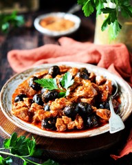 Beef stew with olives and tomatoes on a dark background, rustic