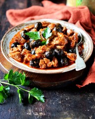 Beef stew with olives and tomatoes on a dark background, rustic