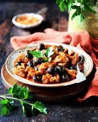 Beef stew with olives and tomatoes on a dark background, rustic