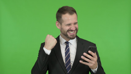 The Cheerful Businessman getting Excited while using Cellphone against Chroma Key