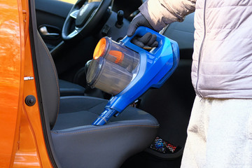 Vacuum cleaner in hands of driver. Cleaning of interior of automobile with blue vacuum cleaner, closeup. Car textile seats is regular cleanup. Horizontal view.