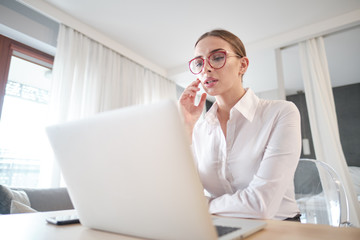 woman in eyeglasses sitting with computer on couch, looking outside, cannot concentrate on work, need some rest, feeling bored, need additional motivation, working remotely at home.