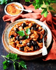 Beef stew with olives and tomatoes on a dark background, rustic