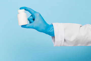 Doctor's hands in sterile gloves hold a jar of pills on a blue background. Infection control concept.