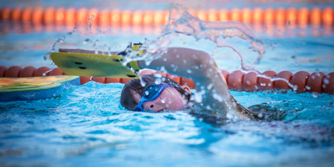 Fototapeta Dziecko aktywnie spędza czas podczas wakacji letnich na kolonii pływając w wodzie na basenie  obraz
