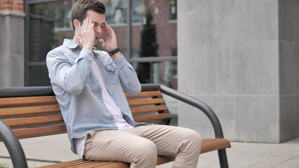 Stressed Casual Young Man with Headache Sitting Outdoor