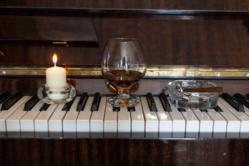 Brandy in glass on  piano key board with cigar in ash tray and burning candle