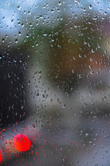 Window overlooking a rainy street. Gloomy evening weather with a view of the road. Drops on glass and bokeh from cars. Stock background for design