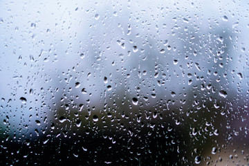 Window overlooking a rainy street. Gloomy evening weather with a view of the road. Drops on glass and bokeh from cars. Stock background for design