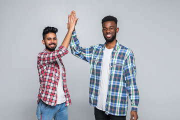 Portrait of a two delighted young men celebrating with high five gesture isolated over gray...