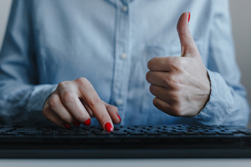 Closeup of woman's hands with red nails typing on a black keyboard showing thumb up like wearing...