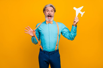 Photo of cool grandpa hold paper air plane recommend new airline show flying good mood wear blue shirt suspenders bow tie pants isolated yellow color background