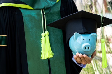 The person in the bachelor uniform  hoding blue piggy bank, Saving money for education plan and...