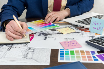 Architects hands drawing of modern apartaments with colour sample and laptop on creative desk, office. Man choosing colors for room decoration.