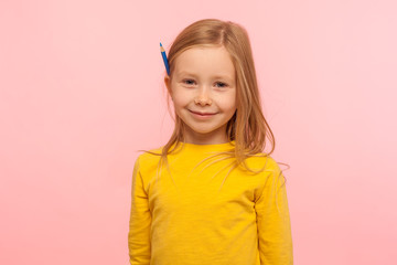 Portrait of charming adorable little girl with ginger hair holding pencil behind ear and smiling to...