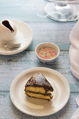 A piece of chocolate and lemon cake on a white plate. Sprinkles on top. Light blue background (clear)