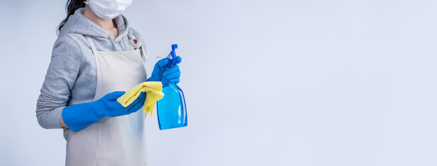 Young woman housekeeper in apron is doing cleaning with blue gloves, wet yellow rag, spraying...