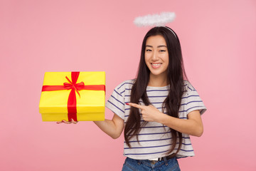 Portrait of positive angelic asian woman with halo over head smiling happily and pointing at gift...