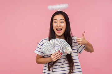 I like my rich life! Portrait of joyful angelic girl with nimbus over head showing thumbs up and...