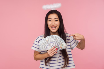 Look at my money! Portrait of glad angelic girl with halo over head pointing at dollars and...