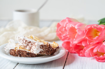 Tiramisu cake, pink tulips and cup of coffee on a white wooden table