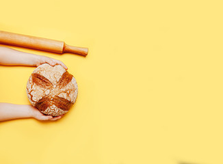 Tasty big round bread in child's hands on yellow background.