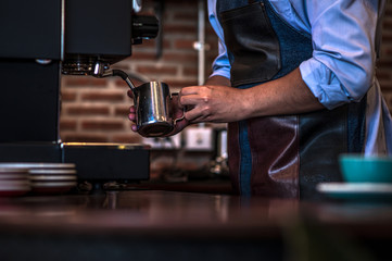 Barista steaming milk at the coffee machine at the coffee shop
